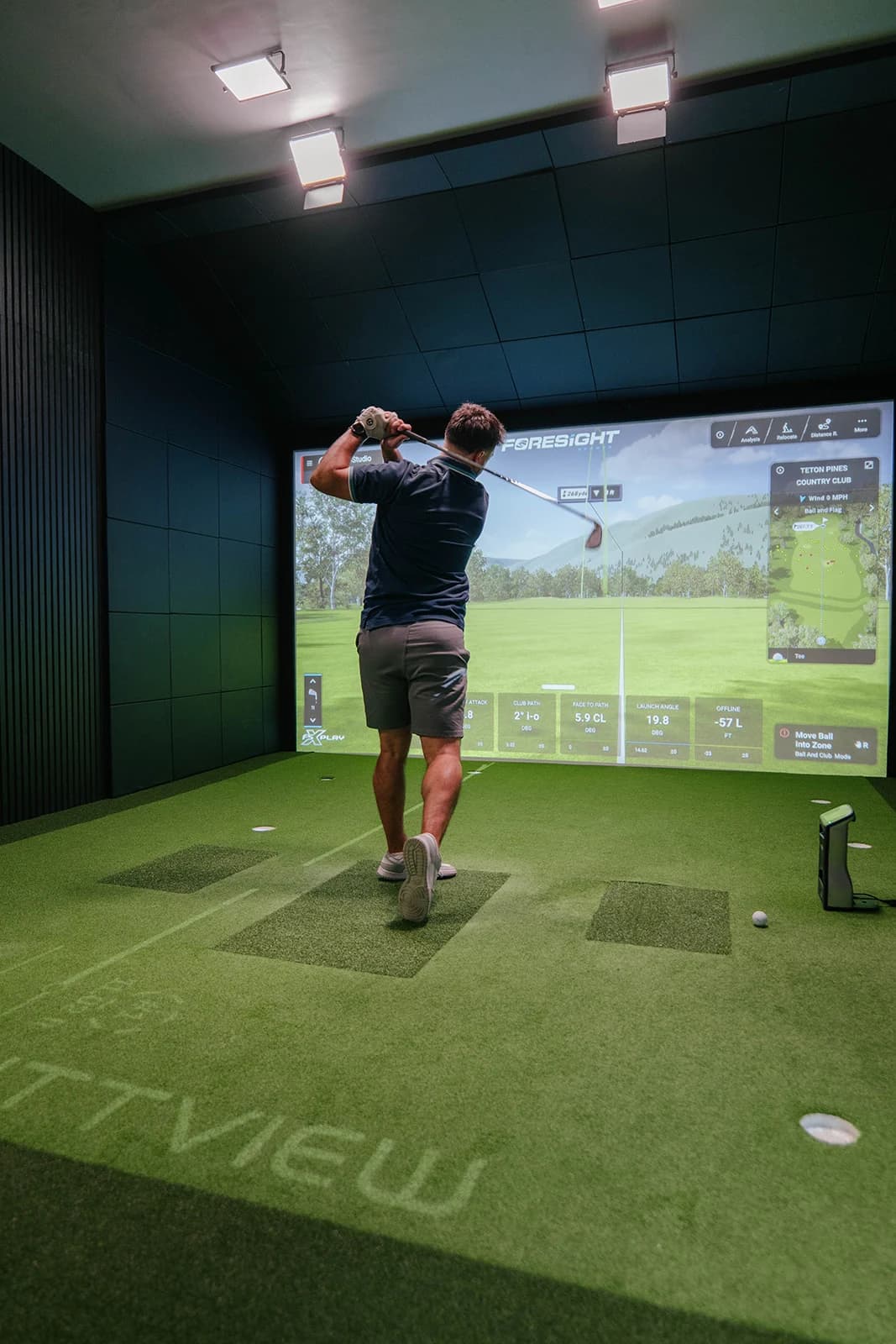 A golfer holds the finish after a shot into the simulator screen, seen from behind